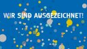 Schriftzug "Wir sind ausgezeichnet" mit Konfetti im Hintergrund