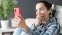Sitzende Frau erschrickt beim Blick auf ihr Handy