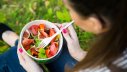 Frau isst Salat aus Einweggeschirr im Park