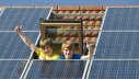 Kinder im Dachfenster freuen sich über Solarzellen auf ihrem Haus