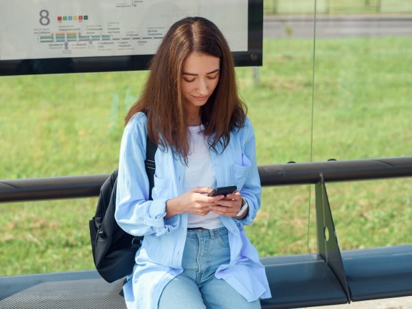 Frau an Bushhaltestelle mit Smartphone