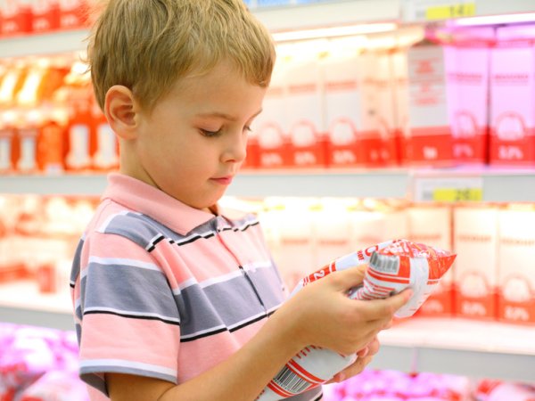 Junge steht vor Kühlregal und schaut sich ein Produkt in seinen Händen an