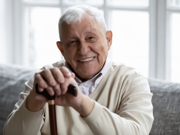 Senior mit Stock sitzt lächelnd auf einem Sofa.