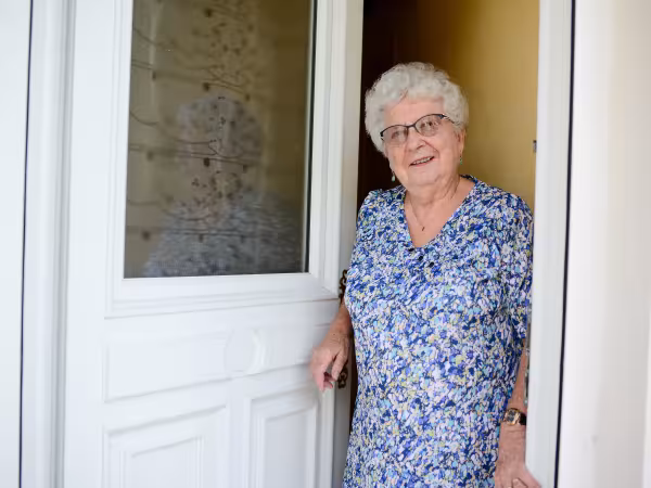 Alte Frau steht an offener Haustür