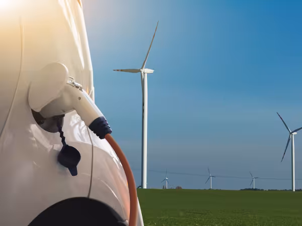 Landschaft mit Elektroauto mit Windrädern im Hintergrund