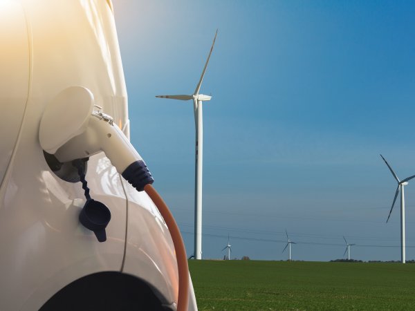 Landschaft mit Elektroauto mit Windrädern im Hintergrund