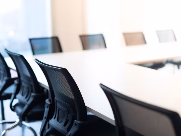 Zu sehen ist die Ecke eines leeren Konferenzraumes an dem schwarze Bürostühle stehen. 