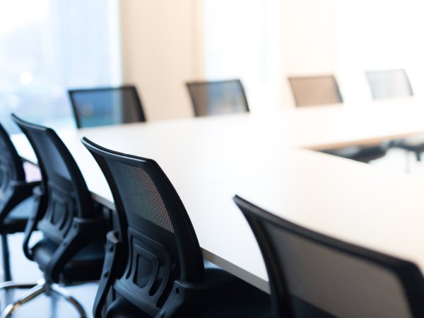 Zu sehen ist die Ecke eines leeren Konferenzraumes an dem schwarze Bürostühle stehen. 