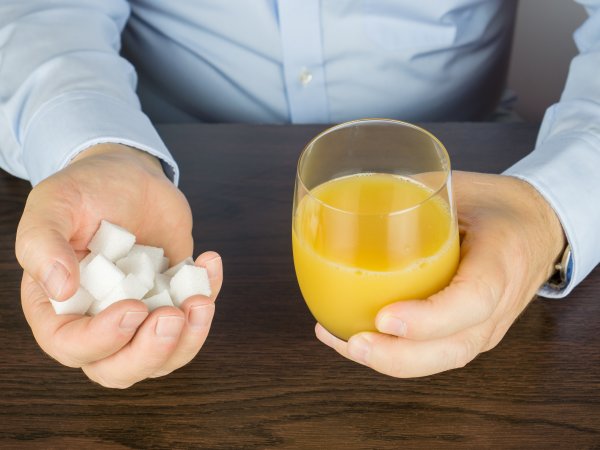 Zuckerwürfel  in der linken Hand, Orangensaft in der rechten Hand