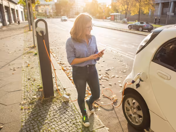 Frau mit Smartphone lädt ein elektrisch angetriebenes Auto