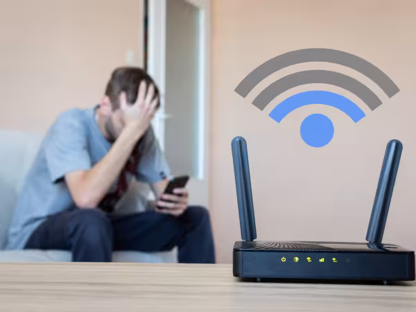 EIn Mann schaut frustriert auf sein handy während der Router geringe Internetgeschwindigkeit anzeigt.