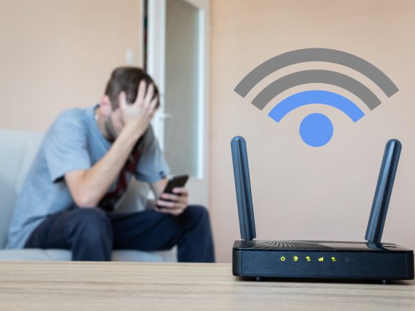 EIn Mann schaut frustriert auf sein handy während der Router geringe Internetgeschwindigkeit anzeigt.