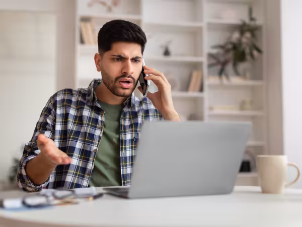 ein Mann telefoniert aufgebracht vor seinem Computer