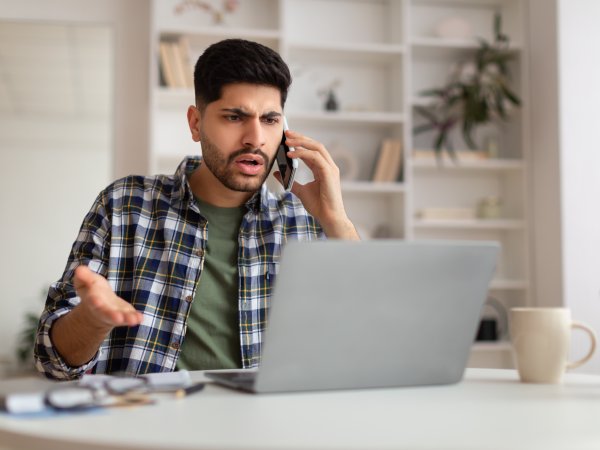 ein Mann telefoniert aufgebracht vor seinem Computer