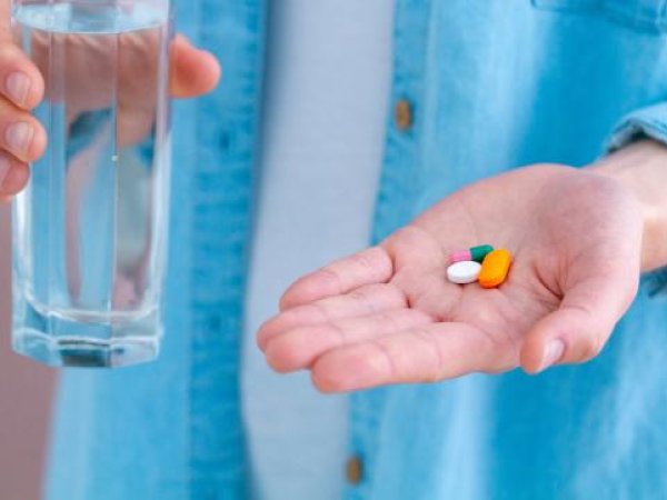 Glas Wasser und Tabletten in der Hand