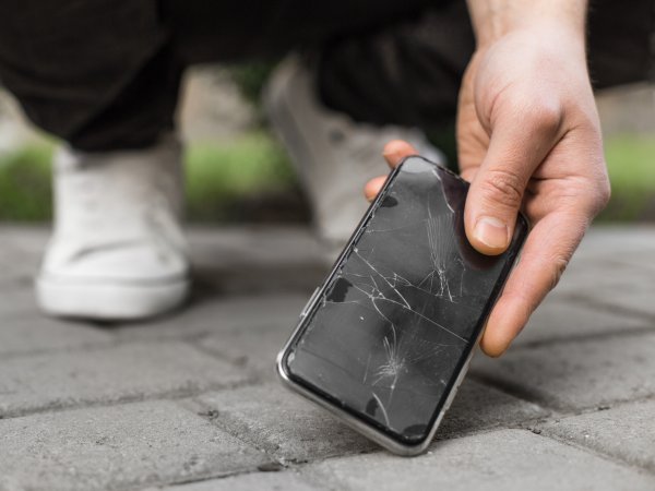 Mensch hebt kaputtes Smartphone vom Boden auf