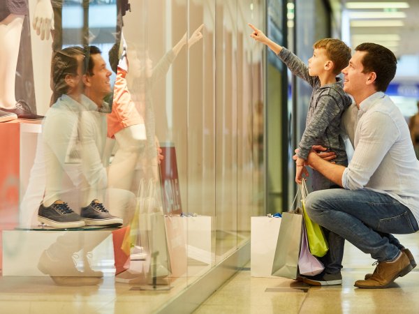 Vater und Sohn knien vor Schaufenster, das Kind deutet auf etwas