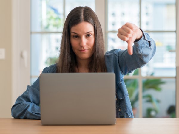 Frau sitzt vor einem Laptop und zeigt mit dem Daumen nach unten.