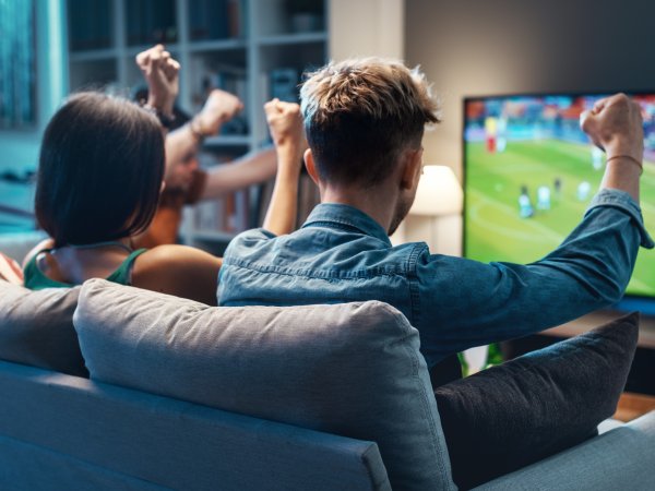 Menschen sitzen auf einem Sofa vor einem Fernseher und schauen Fußball