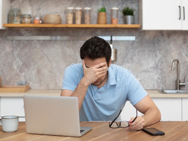 Mann sitzt gestresst mit einer Hand vor dem Gesicht an seinem Laptop
