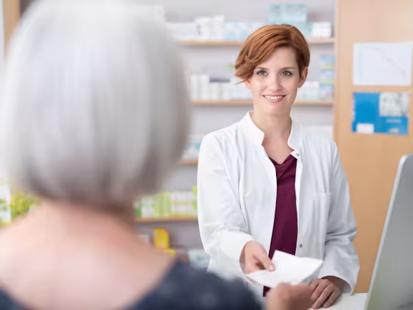 Patientin übergibt ein Rezept an eine Apothekerin