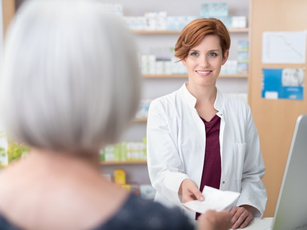 Patientin übergibt ein Rezept an eine Apothekerin