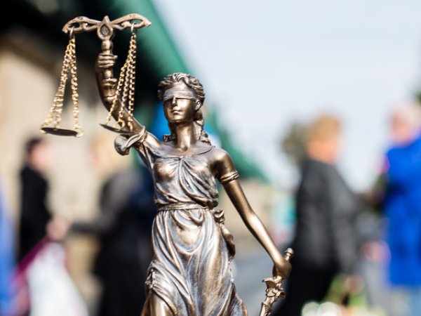 Statue der Justitia, der Göttin der Gerechtigkeit. Eine Menschenmenge im Hintergrund