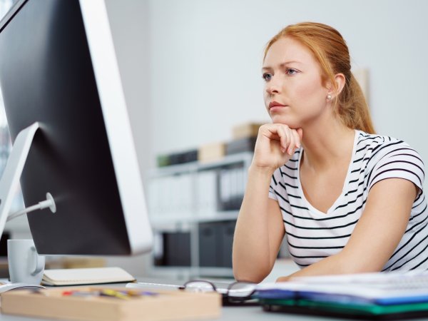 Nachdenkliche Frau schaut auf einen PC-Bildschirm.