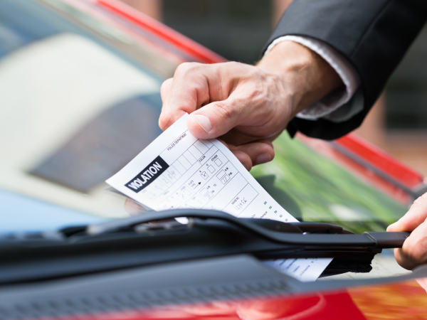 Nahaufnahme eines Mannes, der ein Parkticket auf der Windschutzscheibe des Autos nimmt
