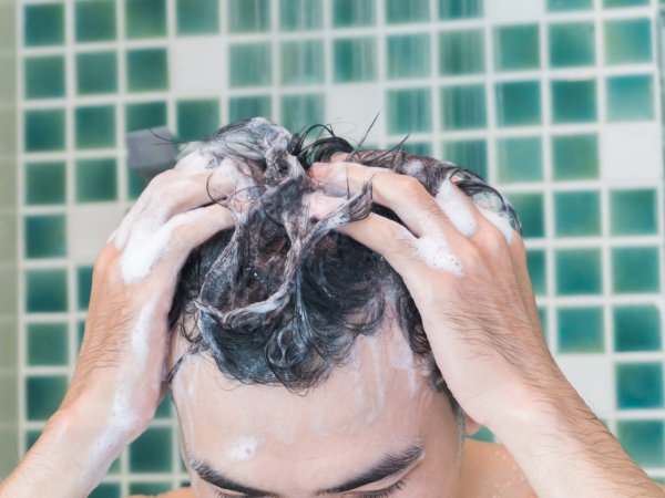 Mann massiert Shampoo unter der Dusche in seine Haare ein