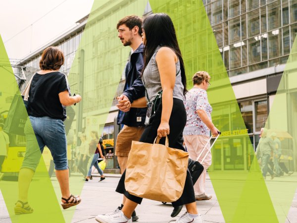 Menschen laufen durch die Innenstadt; im Mittelpunkt des Bildes ist ein Paar zu erkennen; die Frau trägt eine Papiertüte