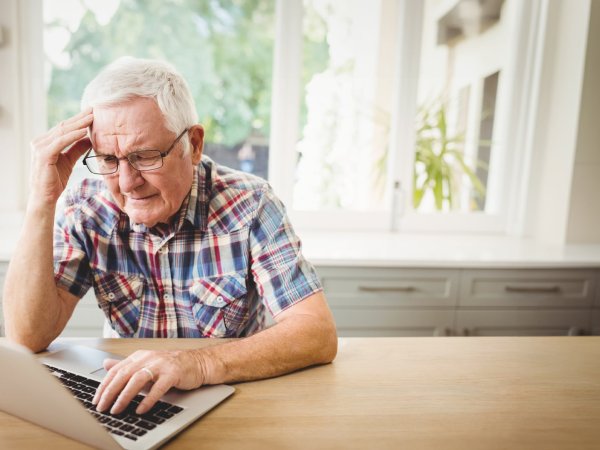 Älterer Mann sitzt am Laptop und sieht verzweifelt aus