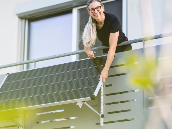 Frau steht auf einem Balkon, an dem ein Solarpanel angebracht ist