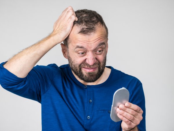 Mann mit lichtem Haar betrachtet seinen Kopf im Spiegel