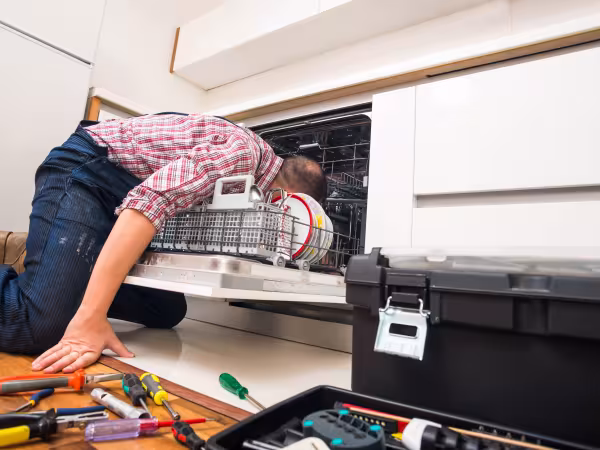 Ein Mann beugt sich in eine Spülmaschine, um diese zu reparieren