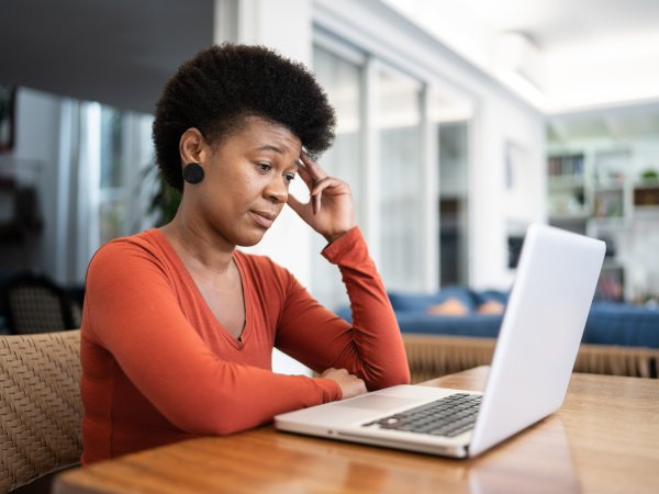Eine Frau sitzt am Tisch und blickt kritisch auf ihren Laptop