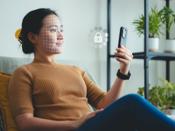 Eine Frau sitzt auf dem Sofa und hält sich für die Gesichtserkennung ein Handy vors Gesicht