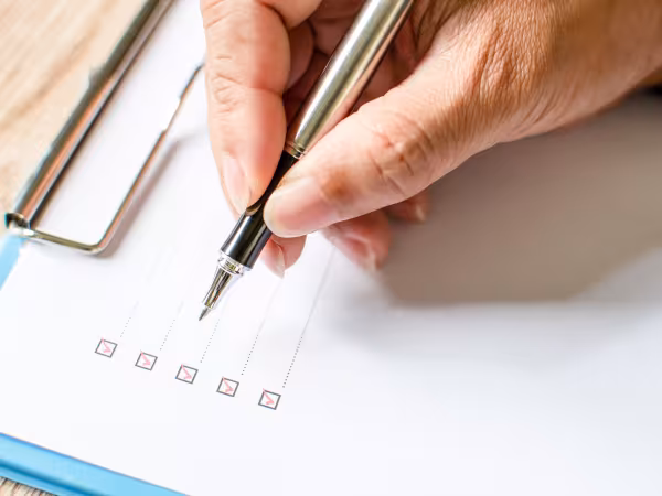 Zu sehen sind in Nahaufnahme die Finger eines Mannes, der einen Stift hält und eine Checkliste abhakt. 