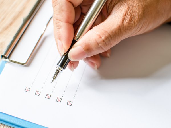 Zu sehen sind in Nahaufnahme die Finger eines Mannes, der einen Stift hält und eine Checkliste abhakt. 
