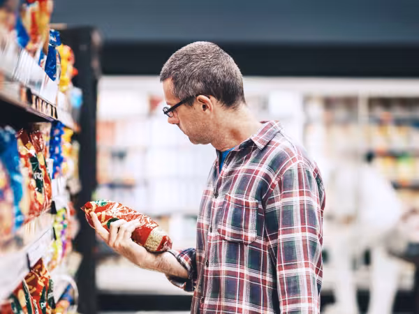 Ein Mann steht im Supermarkt vorm Regal und betrachtet eine Packung, die er in der Hand hält