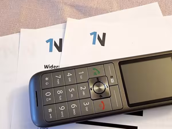 Ein Handy liegt auf Zetteln, auf denen das Logo der Firma 1Ntelecom abgebildet ist
