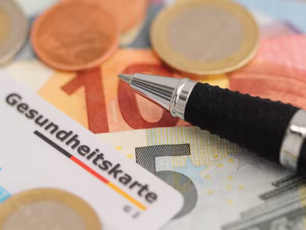 Zu sehen ist eine Gesundheitskarte, Geld und ein Kugelschreiber. 