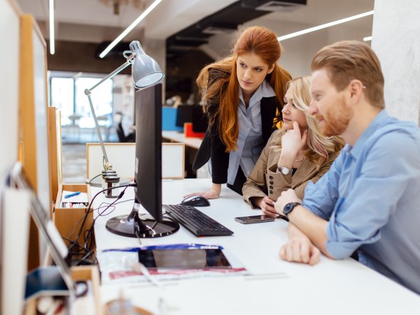 Zu sehen sind drei Kolleg:innen in einem Büro, die gemeinsam auf den Monitor eines Comuters schauen. 