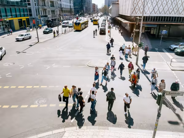 Zu sehen ist aus einer Art Vogelperspektvie ein Platz in Berlin mit Kaufhaus, Passant:innen und öffentlichen Verkehrsmitteln. 