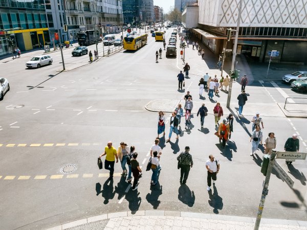 Zu sehen ist aus einer Art Vogelperspektvie ein Platz in Berlin mit Kaufhaus, Passant:innen und öffentlichen Verkehrsmitteln. 