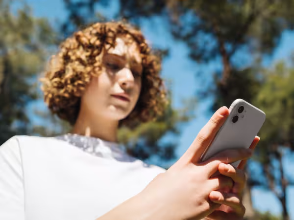 Frau blickt auf Handy, das sie in der Hand hält.