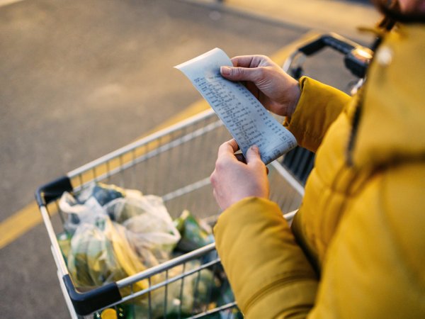 zeigt Mensch in gelber Jacke mit Einkaufsbeleg und Einkaufswagen, Shopping