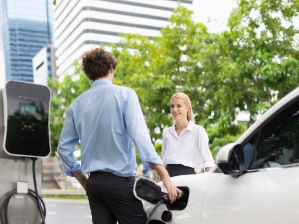 Mann lädt durch E-Ladesäule Elektro-Auto auf und Frau lächelt ihn dabei an