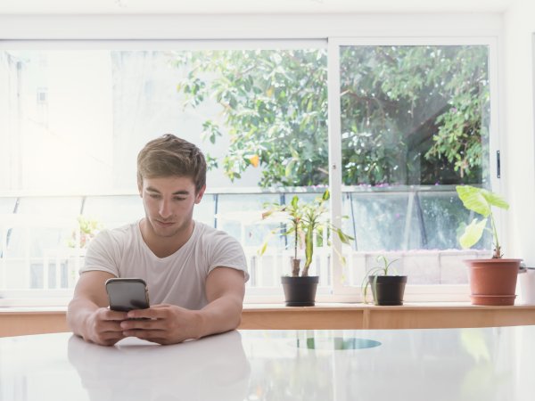 junger Mann sitzt in Küche und schaut auf sein Handy