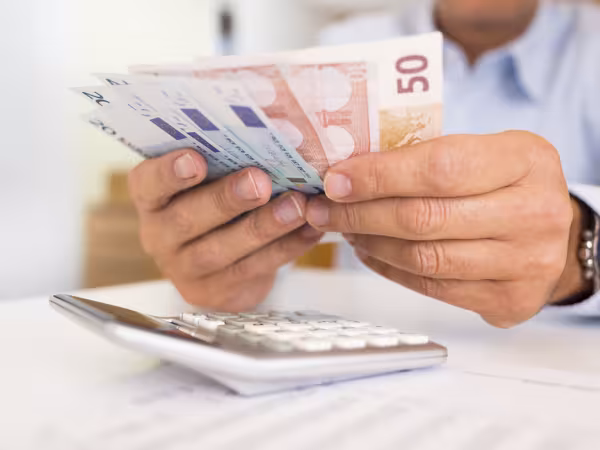Mann hält Geldscheine über einen Taschenrechner